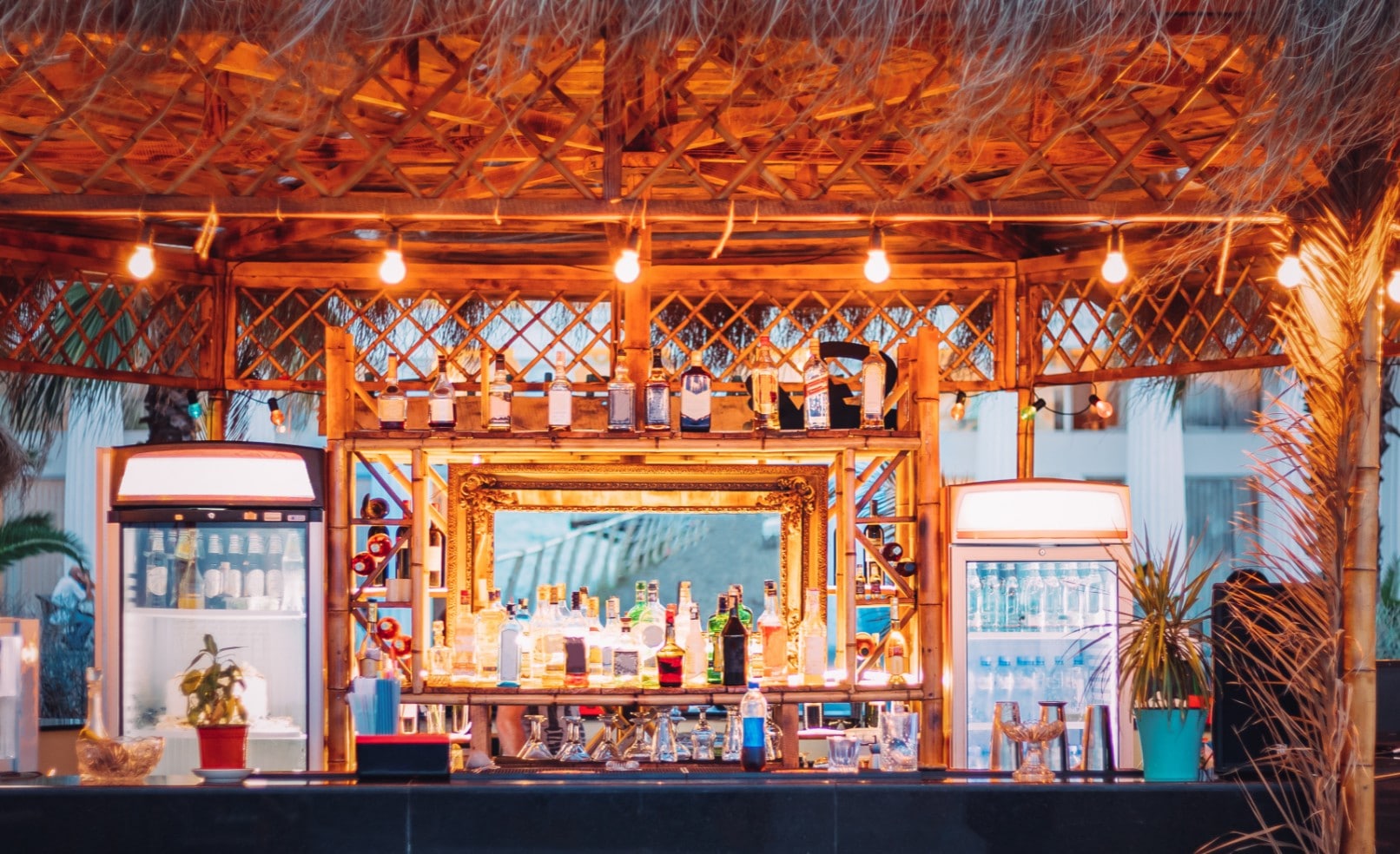 Tropical outdoor bar setup with warm string lights, bamboo accents, and a fully stocked backlit bar area at a vacation rental